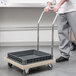 A person pushing a Vollrath dish rack dolly with a grey tray.