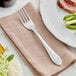 An Acopa stainless steel European table fork on a napkin next to a plate of food.