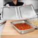 A woman holding a tray of food with a Vollrath hinged steam table cover over meatballs on a counter.