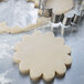 A stainless steel Ateco dahlia flower cookie cutter cutting cookie dough.