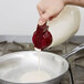 A hand holding a Tablecraft maroon dispenser pouring white liquid into a pan.