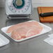 A white CKF foam meat tray with raw chicken breasts on a counter.