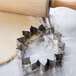 A stainless steel Ateco flower cookie cutter and rolling pin on a table with dough.