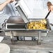 A chef using a Vollrath hinged dome cover on a full size hotel pan to cook food on a table