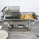 A Vollrath hinged dome cover on a stainless steel chafing dish with food.