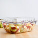 A clear Cambro deli crock lid on a glass dish with fruit in it.