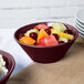 A Tablecraft maroon speckle cast aluminum serving bowl filled with fruit salad on a table in a salad bar.