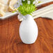 An Acopa bright white porcelain bud vase with flowers on a table.