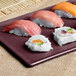 A Tablecraft maroon speckle rectangular cooling platter with sushi on a table.