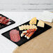 Two black Tablecraft rectangular cast aluminum cooling platters with food on them.