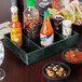 A black HS Inc. condiment organizer holding jalapenos, salsa, hot sauce, and other condiments on a table.