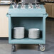 A slate blue Cambro dish cart with trays and bowls on it.