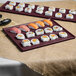 A maroon speckled rectangular metal cooling platter with sushi on a table.