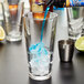 A Libbey mixing glass with ice and blue liquid being poured into it.