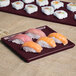 A maroon speckled rectangular cast aluminum cooling platter with sushi on a table.