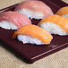 A Tablecraft maroon speckle rectangular cast aluminum platter with sushi on a table.