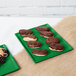 A green Tablecraft cast aluminum rectangular platter with chocolate covered pastries on a table.