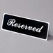 A white table with a black and white Vollrath 9" x 3" table tent sign that says "Reserved"
