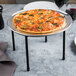 A pizza on a Clipper Mill black iron round 1-tier pizza stand on a table.