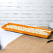 A Tablecraft orange rectangular cast aluminum tray with food on it.