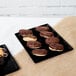 A Tablecraft black cast aluminum rectangular cooling platter holding chocolate covered donuts on a table in a bakery display.