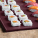 A Tablecraft maroon speckle metal rectangular platter with sushi on a table.
