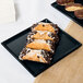 A Tablecraft black cast aluminum rectangular cooling platter with chocolate covered pastries on a table.