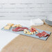 A Tablecraft gray cast aluminum rectangular cooling platter holding meat and cheese on a table with white plates.
