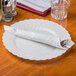 A white plate with a silver knife and fork on a silver Hoffmaster dinner napkin.