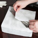 A hand placing a Hoffmaster Silver Prestige Linen-Like dinner napkin on a table with a fork.
