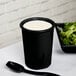 A Tablecraft black cast aluminum salad dressing crock with a black spoon in it on a table with salad.