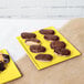 A chocolate covered doughnut on a yellow Tablecraft rectangular cooling platter.