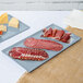 Two gray cast aluminum Tablecraft rectangular cooling platters with meat and cheese on a counter.