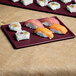 A rectangular maroon speckle cast aluminum Tablecraft cooling platter with sushi on it.