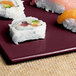 A Maroon speckled rectangular cast aluminum platter with sushi on it.
