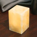 A Sterno alabaster square liquid candle holder with a yellow candle on a wooden table.