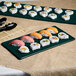 A Tablecraft hunter green and white speckled cast aluminum rectangular cooling platter with sushi on a table.