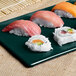 A Tablecraft hunter green and white speckled cast aluminum rectangular cooling platter holding sushi on a table.