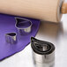 A silver Ateco stainless steel comma cutter set and a rolling pin on a purple surface.