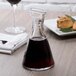 A Stolzle Pisa carafe filled with red wine on a table next to a plate of food.