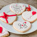A heart shaped cookie decorated with a red heart next to other heart shaped cookies on a plate.