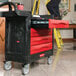 A man standing next to a black Rubbermaid TradeMaster tool cart with red drawers.