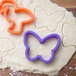 A purple butterfly-shaped Wilton cookie cutter on a piece of dough.