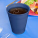 A navy blue plastic cup on a blue table with a cup of liquid.