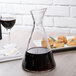A Stolzle glass carafe filled with dark liquid on a table next to a plate of food.