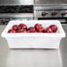 A white Choice plastic food storage container filled with red apples on a counter.