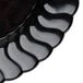 A close-up of a Fineline Flairware black plastic plate with a scalloped edge.