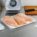 A white foam CKF meat tray filled with raw chicken breasts on a table.