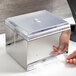 A hand opening a silver box containing a clear Vollrath Straw Boss lid.