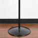 A Marco Company black metal floor mount produce bag stand with a black pole.